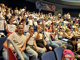 Das Foto zeigt die Chorkids bei dem Konzert; die Schülerinnen blicken in die Kamera und zeigen ihre Freude und Begeisterung.