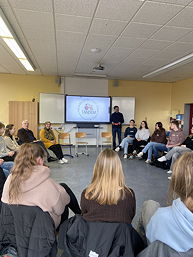 Das Foto zeigt einen Blick in den Klassenraum mit dem Referenten und der Referentin; die Schülerinnen und Schüler sitzen im Kreis; auf der digitalen Tafel ist im Hintergrund das Logo der Veranstaltung zu sehen.